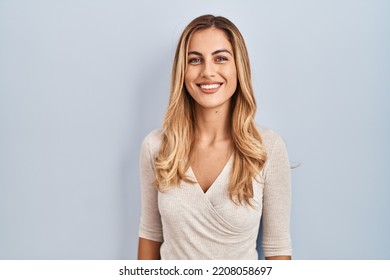 Người phụ nữ trẻ tóc vàng đứng trên nền xa xôi với nụ cười vui vẻ và thoải mái trên khuôn mặt. Người may mắn.