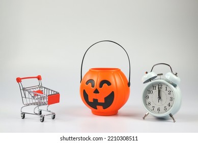Front view of  Halloween pumpkin bucket  with shopping cart and white vintage alarm clock 12 pm. isolated  on white  background with copy space. Halloween holiday midnight shopping  concept.