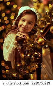 Joyful little girl stands on the staircase in fabulous Christmas setting in a nightie and a cap and  smiles cutely. Vintage style. Christmas and New Year concept. 