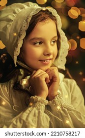 Christmas miracles and dreams. Portrait of a joyful little girl in a nightie and a nightcap standing in a festively decorated  room surrounded by flickering lights. Magic Christmas. Vintage style. 