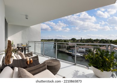 Prachtig uitzicht vanaf luxe balkon in terracotta kleuren, elegante en moderne meubels in rieten en metaal, glazen balustrade, uitzicht richting de baai van Miami met luxe huizen met jachten en parken