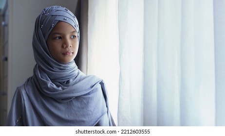 Anak Muslim Asia 10 tahun berdiri di samping jendela.Gadis muslimah cantik berhijab dan kostum tradisional.Konsep potret orang Muslim.