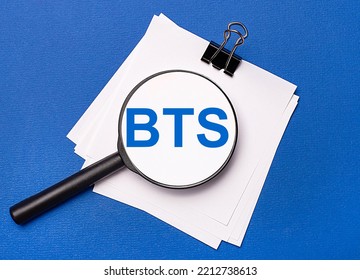 Sobre fondo azul, hojas blancas debajo de un clip negro y sobre ellas una lupa con el texto BTS Customer Relationship Management