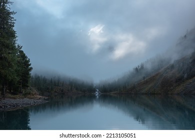 雲の中に雪の城がある静かな風景。マウンテン クリークは、森の丘から氷河湖に流れ込みます。霧のクリアランスの雪山。穏やかな高山湖に映る小さな川と針葉樹。