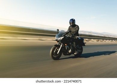 Vista laterale di un motociclista in sella a una moto da corsa su uno sfondo di mare con sfocatura del movimento