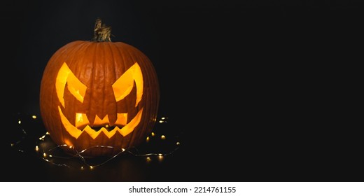 Real Halloween orange pumpkin in black background with fairy lights giving spooky season vibes. Scary pumpkin head portrait glowing inside with orange lights, October 16, 2022.