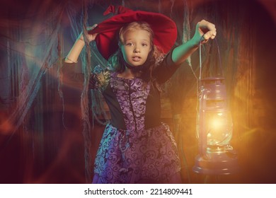 魔女の衣装を着たかわいい子供の女の子が、手にランタンを持って暗い古城に立っています。ハロウィンの飾り付け。ハロウィンのおとぎ話。