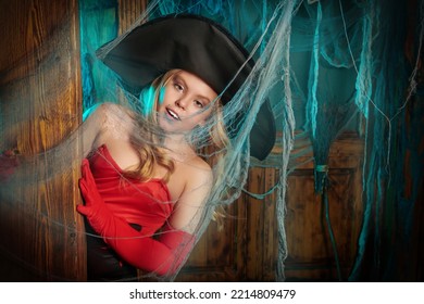 ハロウィンの話。魔女の衣装を着たかなり金髪の女の子が、恐ろしいクモの巣に囲まれた古い家に立っています。ハロウィンの飾り付け。