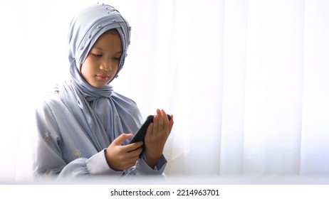 10 歳のアジアのイスラム教徒の子供が窓のそばに立っています。インターネット デバイスを使用して、ヒジャブと伝統的な衣装を着た美しいイスラム教徒の少女。
