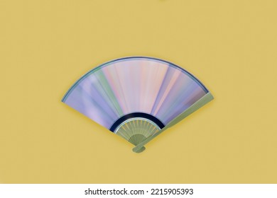 Traditional hand holding fan with compact disc with rainbow reflections. Diffraction of light into iridescent pastel pink-blue-purple-green-orange spectrum. Minimal abstract musical concept. Flat lay.