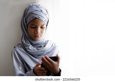10 歳のアジアのイスラム教徒の子供が窓のそばに立っています。インターネット デバイスを使用して、ヒジャブと伝統的な衣装を着た美しいイスラム教徒の少女。