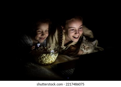Two sister girls with a cat watch cartoons on the device and have a fun together. They're at home. Childhood. Leisure.