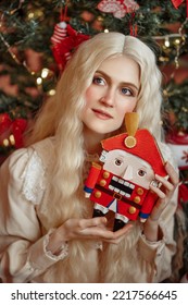 Portrait of a beautiful white-haired girl with a Nutcracker in her hands against the backdrop of a Christmas tree. New Year. Christmas. Fairy tale for real.