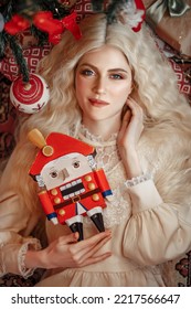 Portrait of a beautiful white-haired girl with a Nutcracker in her hands against the backdrop of a Christmas tree. New Year. Christmas. Fairy tale for real.