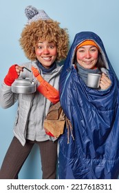 Happy women campers enjoy travel holiday in winter drink tea smile gladfully have frozen face on frost wear warm clothes wrapped in sleeping bag carry wood pose indoor. Adventure wanderlust lifestyle