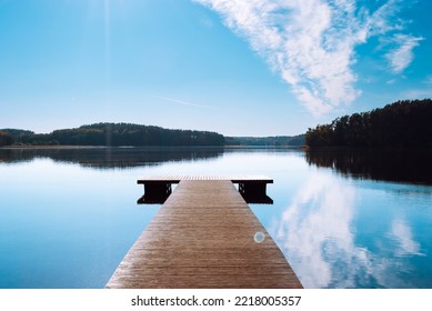 Ein Holzsteg vor der Kulisse eines Sees mitten im Wald. Blauer Himmel mit Wolken, die sich im Wasser des Sees Baltieji Lakajai im Regionalpark Labanoras widerspiegeln.