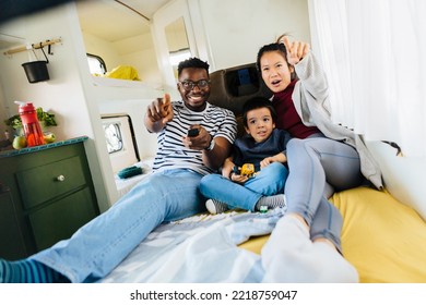 楽しい家族がキャンピングカーのベッドに横たわり、テレビで映画や漫画を見ています。母親はテレビを指さし、父親はリモコンを持っています。