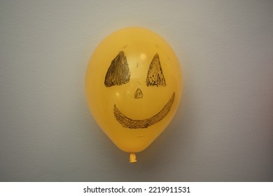Happy Halloween. One orange scary balloon hangs on wall, painted by children for holiday. Different emotions of joy, anger, laughter. Festive design, party concept