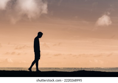 Man with head down walking alone outdoors silhouette