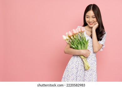 분홍색 배경에 고립된 꽃다발을 들고 있는 드레스를 입은 예쁜 미소 짓는 아시아 여성