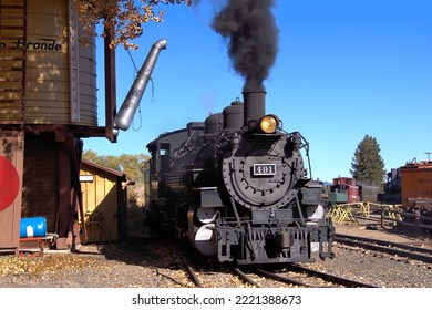 Antike Dampflokomotive 491 neben einem Eisenbahnwasserturm mit dunkelschwarzem Rauch