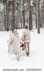 Me encanta la joven pareja romántica, el chico en el bosque de invierno frío y cubierto de nieve caminando con una mascota, el perro de raza de caza borzoi ruso. Lebrel, dueño de un perro lobo. Divertirse, reír. Abrigo de piel con estilo, gorro de lana.