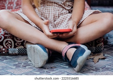 Una bambina carina è seduta in una posizione non salutare e usa un telefono cellulare. Danni alla salute causati dai dispositivi elettronici