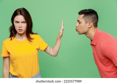젊은 커플 두 친구 가족 남자 여자가 기본 티셔츠를 함께 입고 남자가 여자에게 키스를 원하지만 그녀는 손바닥 제스처를 멈추고 원하지 않는다. 파스텔 단색 밝은 녹색 배경에 고립되어 있다.