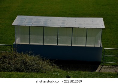 サッカー場のガラス プラスチック シェルター。スポーツスタジアムエリアの芝生のプレキシガラス更衣エリア。金属製の梁で作られたプラスチック アクリル ガラス ストップ待合室