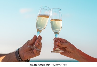 美しいサンセット ビーチを背景にワイングラスで乾杯。カップルはシャンパンを持ち、休日を祝います。時計を持つ男の手。