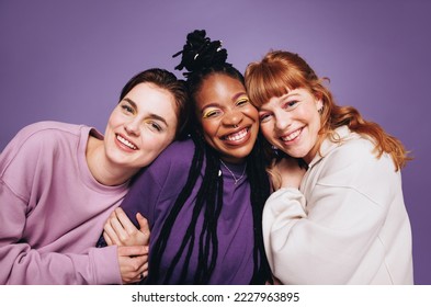 Retrato de amigas felizes sorrindo para a câmera em um estúdio. Melhores amigas se divertindo enquanto estão de pé contra um fundo roxo. Três jovens mulheres criando memórias felizes juntas.
