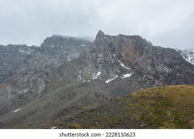 Dramatische Landschaft mit scharfem Gipfel auf einem hohen Gebirgszug in regnerischen, tief hängenden Wolken. Trostlose Alpenlandschaft mit spitzem Berggipfel in einem niedrigen, grauen, bewölkten Himmel. Düsterer Blick auf einen großen, spitzen Gipfel in grauen Wolken.