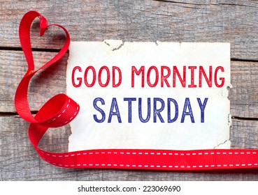 Good Morning Saturday. White card with text Good Morning Saturday on wooden table, with red ribbon 