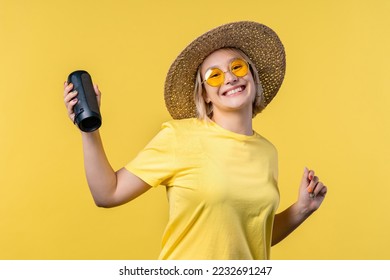 Young woman listening to music by wireless portable speaker - modern sound system. Lady dancing, enjoying on yellow studio background. She moves to rhythm of music.