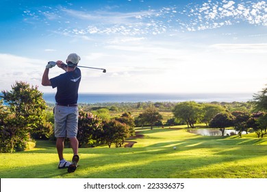 Hombre golpeando una pelota de golf colina abajo hacia el océano y el horizonte