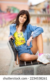 Retrato de una hermosa joven modelo sentada en un banco al aire libre en la ciudad
