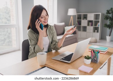 Zdjęcie zadowolonej asystentki agenta nieruchomości rozmawiającej przez telefon przeglądającej netbooka wybierającej mieszkanie dom apartament siedzącej w biurze domowym w pomieszczeniu stanowisko pracy