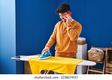 شاب إسباني يتحدث على الهاتف الذكي أثناء كي الملابس في غرفة الغسيل