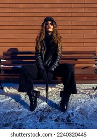 señora atractiva se sienta en el banco al aire libre. Modelo de moda posando al aire libre en invierno.