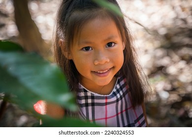 The face of asian little girl surrounded by tropical leaves. Closeup portrait of a beautiful swarthy baby with tan skin and dark hair.