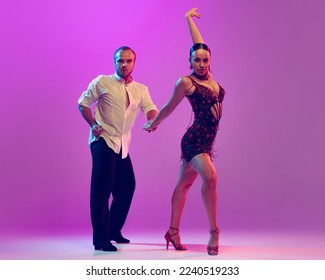 Elegance. Two young graceful dancers wearing stage outfits dancing ballroom dance isolated on purple background. Concept of art, dance, beauty, music, style. Copy space for ad