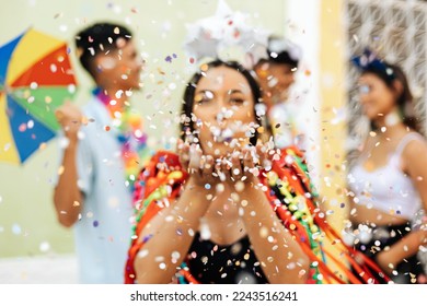 Brasilianesche Karneval. Grupp vu Frënn feiert Karnevalsparty. Selektiv Fokus vun enger Fra, déi Konfetti bléist.