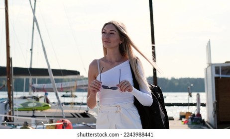 A blonde woman walks along the pier to sail on a yacht moored to the pier.