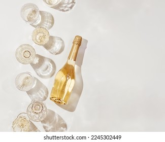 Composición plana con una botella de vino espumoso blanco y copas de vino con sombras y destellos de sol sobre un fondo beige claro. Fotografía estética de vino blanco con espacio de copia. Bodegón monocromático de vacaciones de verano.