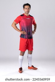 Futbollist mashkull i veshur me uniformë dhe këpucë atletike, në këmbë në këmbë, qëndrim i sigurt sipas personalitetit të atletit në një sfond të bardhë në studio.