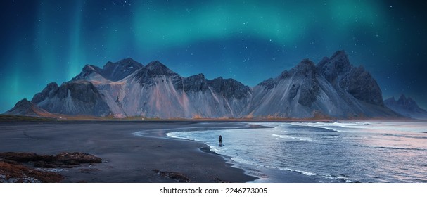 Verbazingwekkende IJslandse natuurzeegezichten. Iconische locatie voor landschapsfotografen en bloggers. Schilderachtig beeld van IJsland. Alleenstaande toerist tegen de Vestrahorn-berg met groen noorderlicht en reflectie