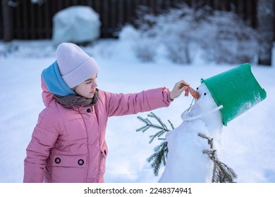 Klein meisje maakt sneeuwpop op ijzige winterdag. Kind maakt neus van wortel. . Foto van hoge kwaliteit