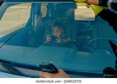 Close up of young boy excited while playing video game in passenger seat and dad wiping car window