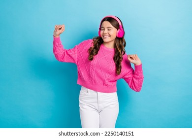 Photo of young dancing satisfied teenager schoolgirl wear new wireless pink headphones hands up active dance isolated on blue color background