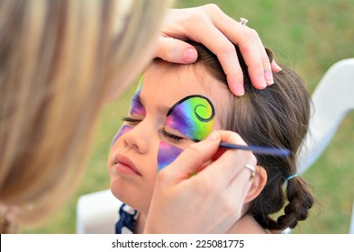 Young girl (age 5-6) getting her face painted like a butterfly by face painting artist. Real people. Copy space